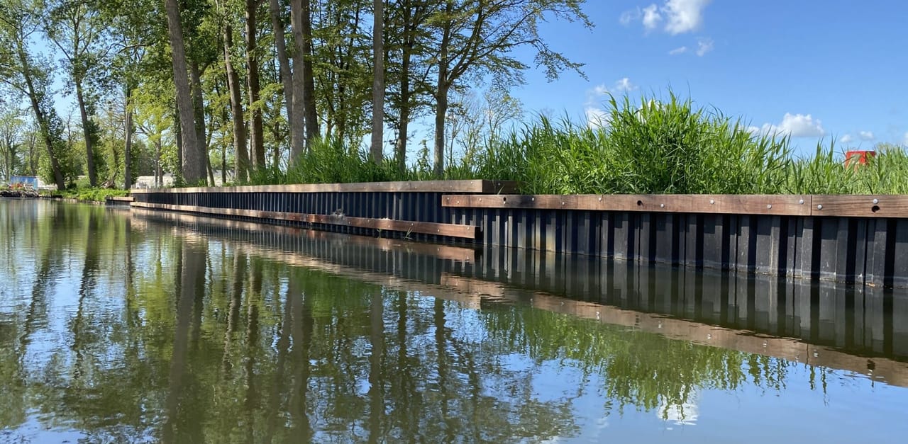 Aangelegde waterkant met donkere kunststof damwand en houten gording